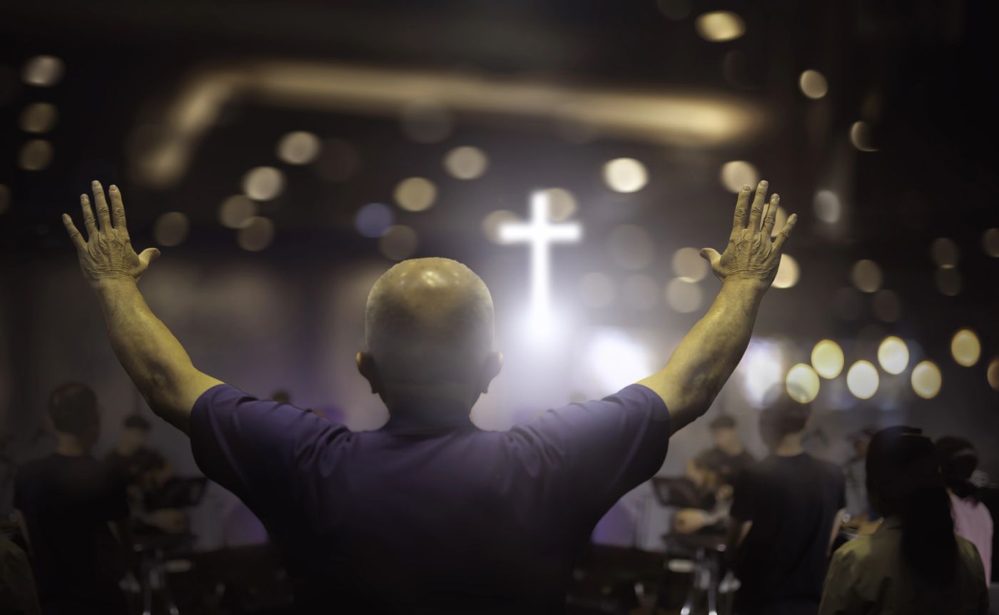 A man worshiping with hands raised toward a lit cross